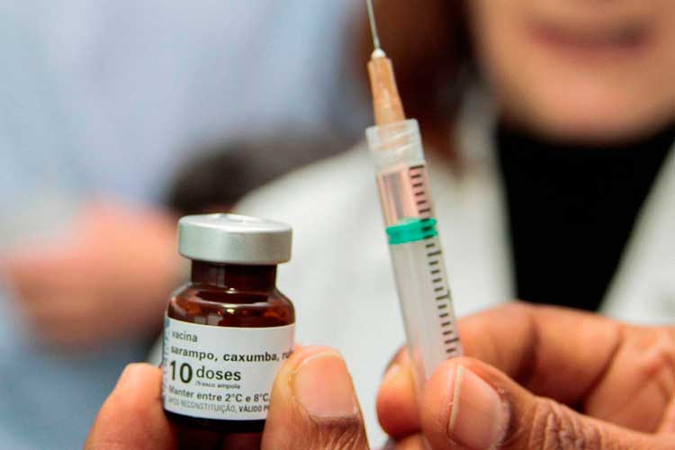 Pessoa segura ampola de vacina contra sarampo, caxumba e rubéola