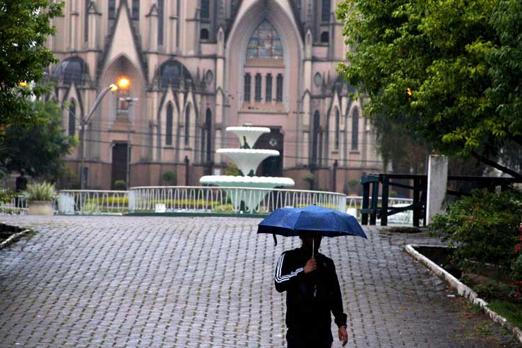 Homem segurando guarda-chuva azul em frente à Catedral de Santa Cruz do Sul